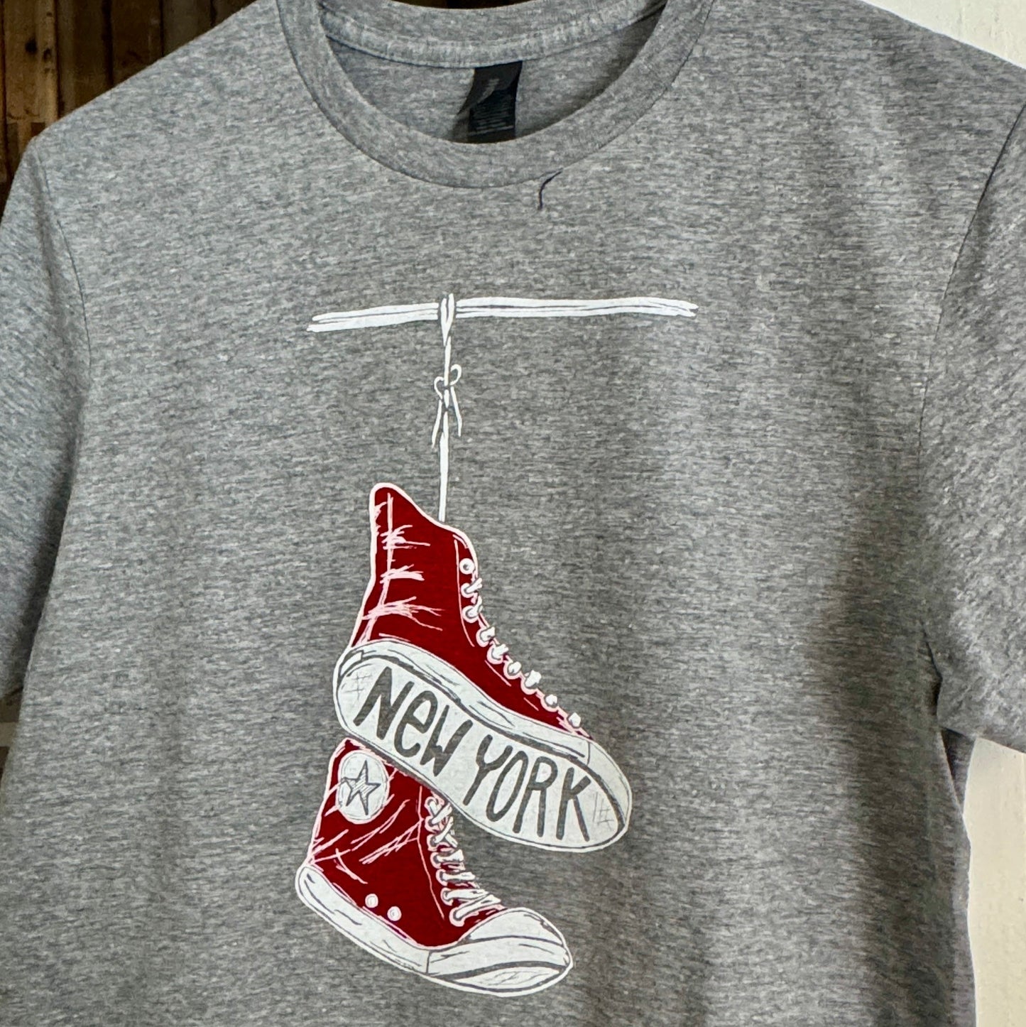 Gray t-shirt with a red shoe graphic and 'New York' text on a hanger.