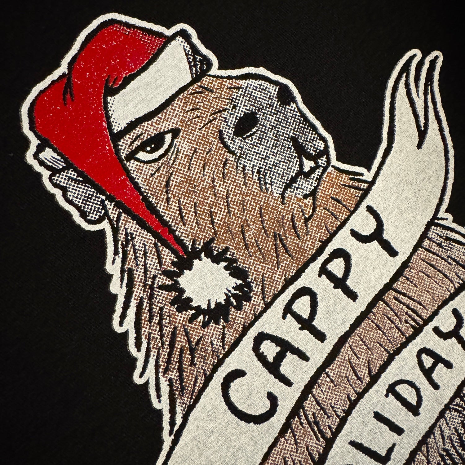 Black t-shirt with a graphic of a capybara wearing a Santa hat and a banner reading 'Cappy Holidays'.