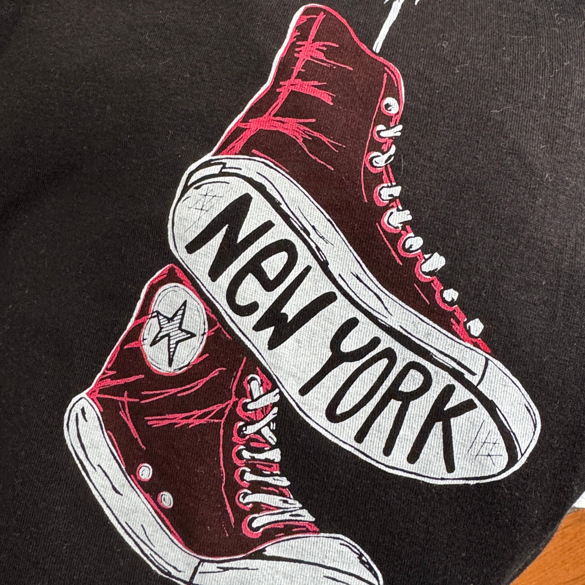 Black sweatshirt with red and white sneakers graphic and 'New York' text on a hanger.