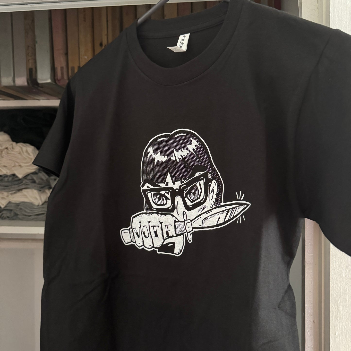 Black t-shirt with a graphic design of an anime girl with glasses holding a knife on a hanger.