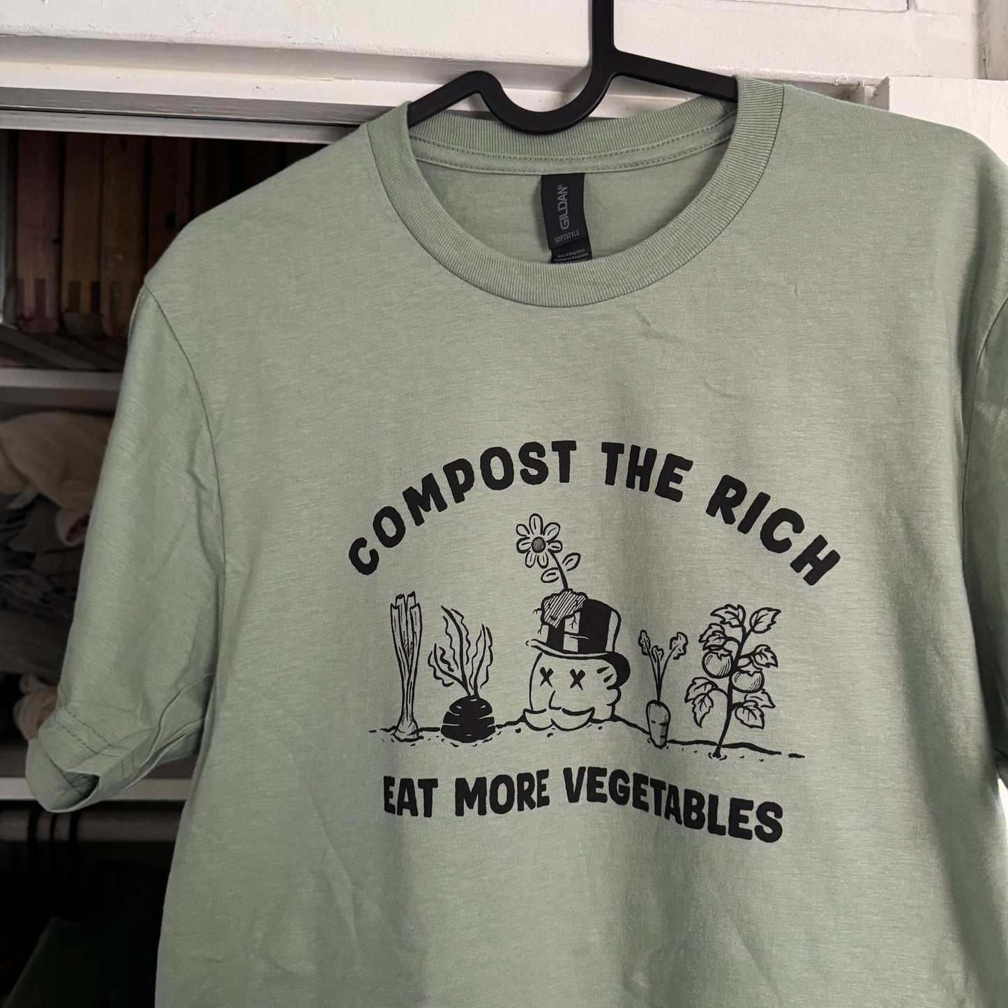 Light green t-shirt with compost-themed design on a rack.