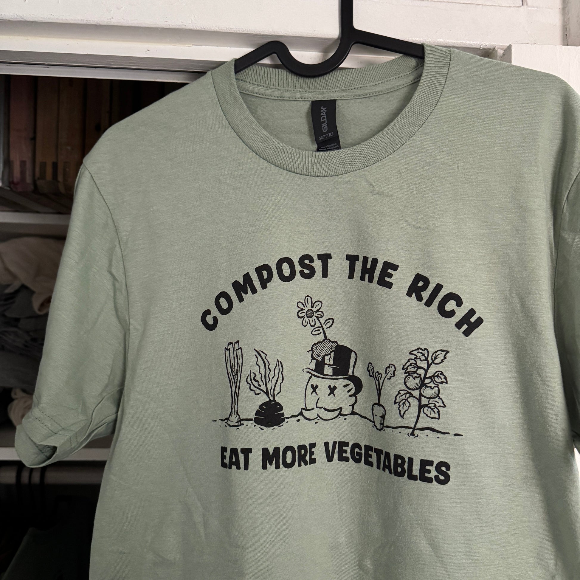 Light green t-shirt with compost-themed design on a rack.