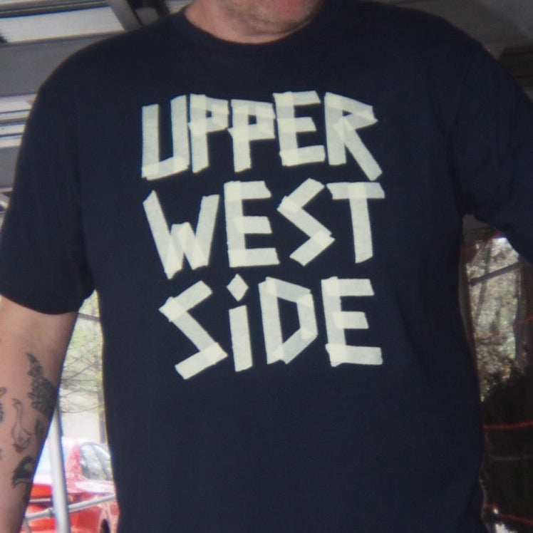 Person wearing a 'Upper West Side' masking tape printed shirt holding a phone in new york city