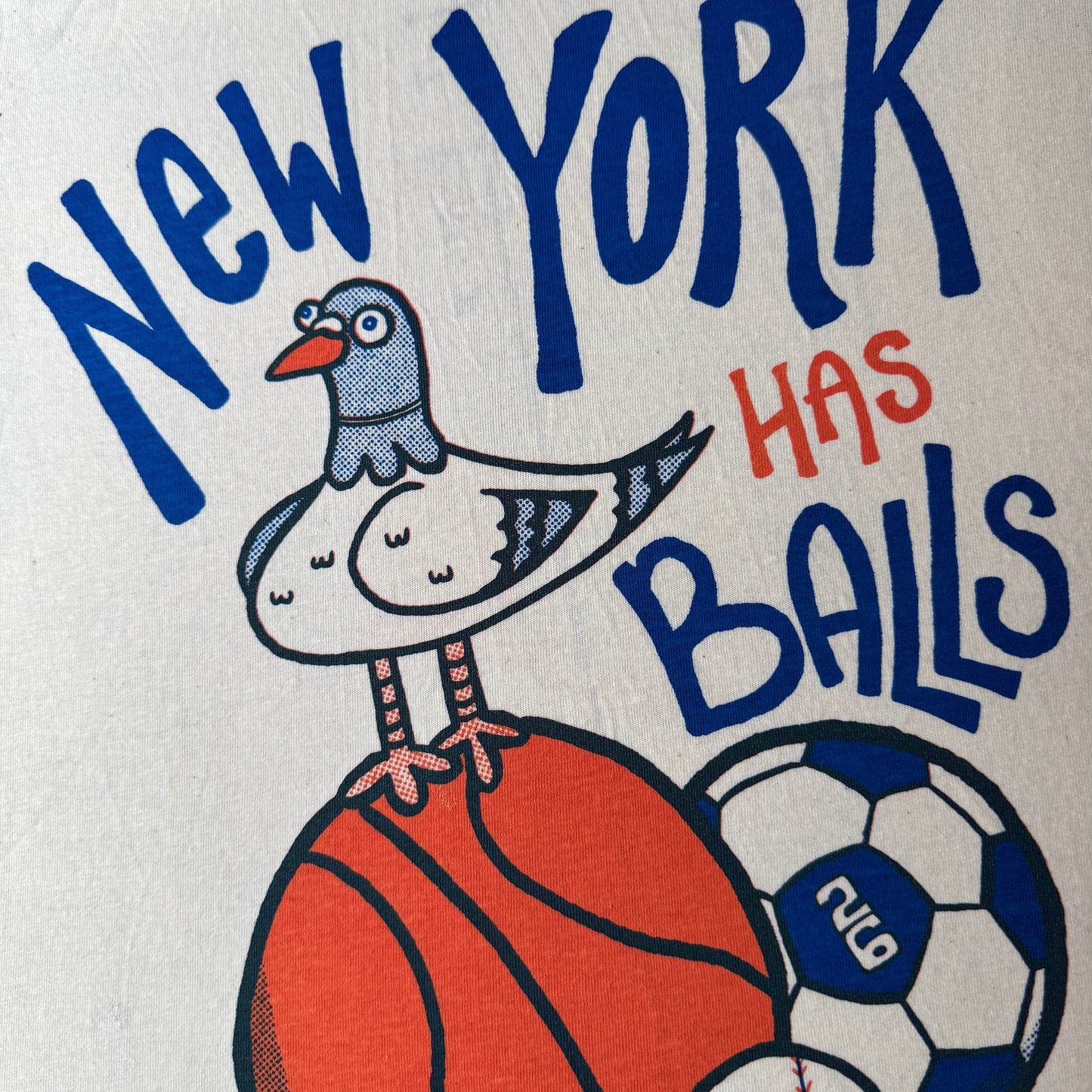 T-shirt with 'New York Has Balls' text and a pigeon with sports ball graphics on a vintage white shirt