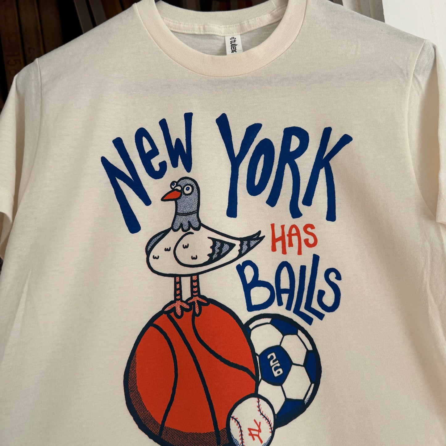 T-shirt with 'New York Has Balls' text and a pigeon with sports ball graphics on a vintage white shirt