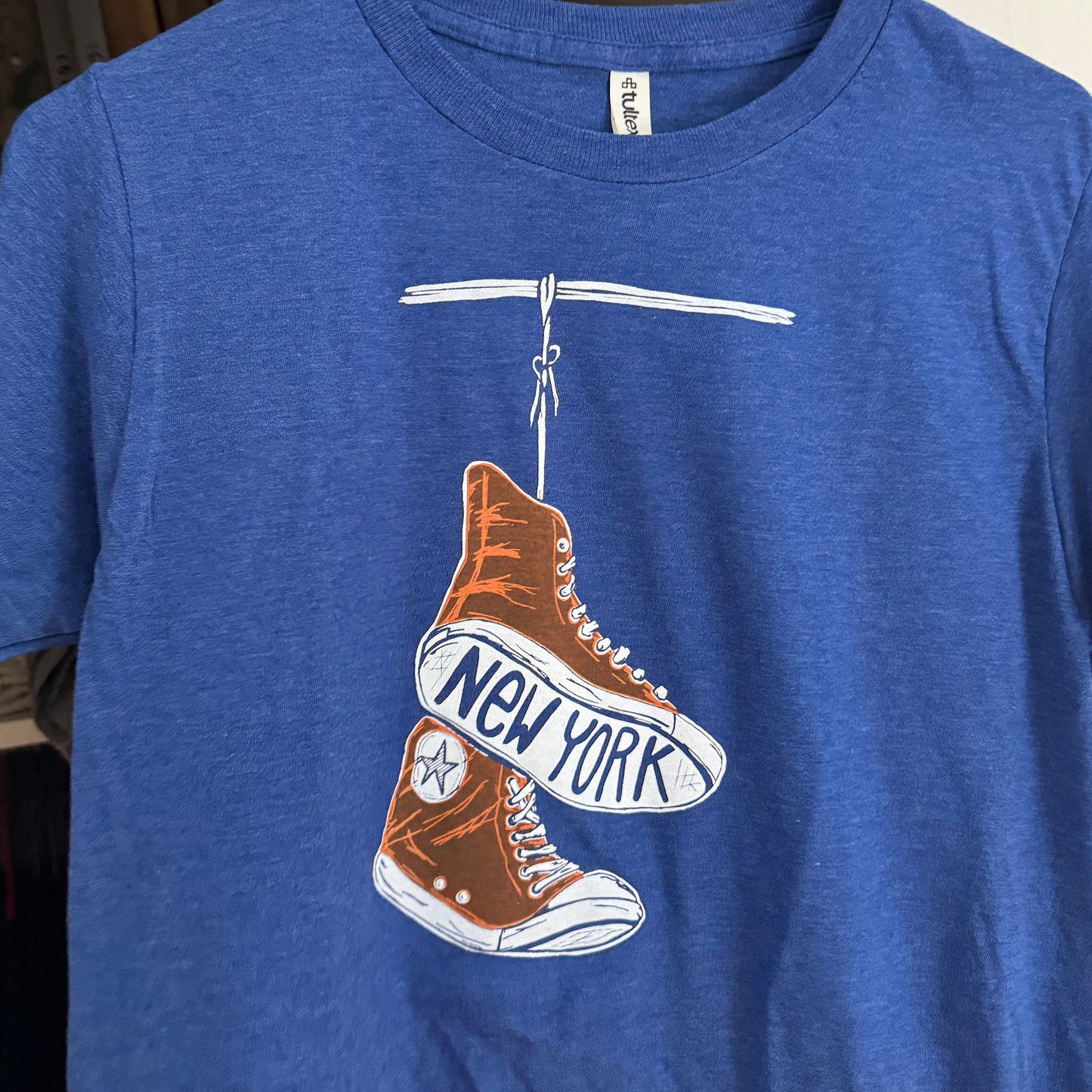 Illustration of a orange NY KNICKS converse sneakers with 'New York' text on the sole on a blue t-shirt