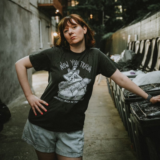 Man wearing a dark t-shirt with New York City Raccoon design and text, standing next to garbage.