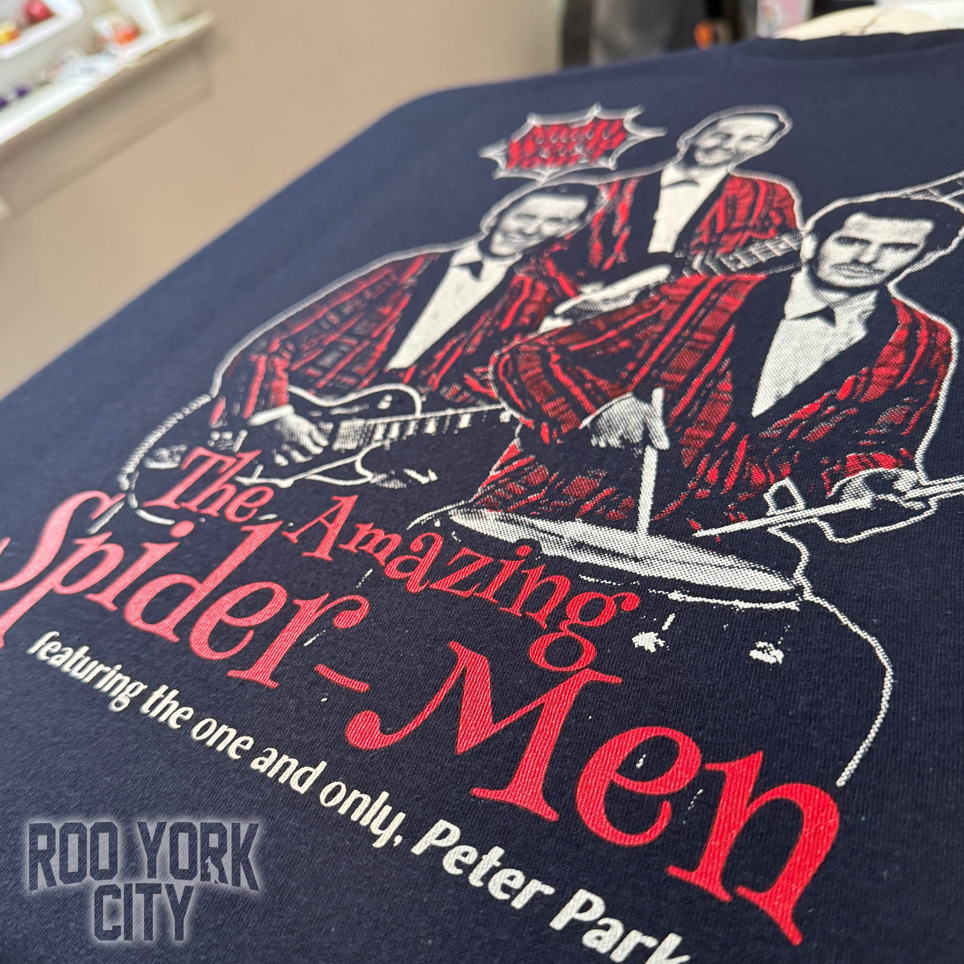 Image of the 3 Spider-Man actors put together as a rock band in red plaid suits with guitars, featuring text 'Multi World Tour' hand printed on a dark t-shirt.